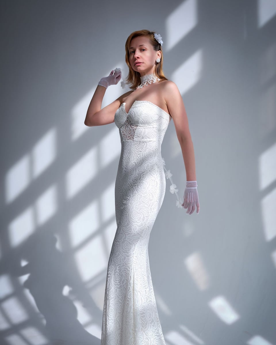 Illustrative photograph of a bride in a lace gown and gloves against a softly shadowed wall.