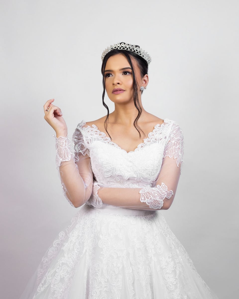 Illustrative studio photograph of a bride in a white lace gown and tiara looking to one side.