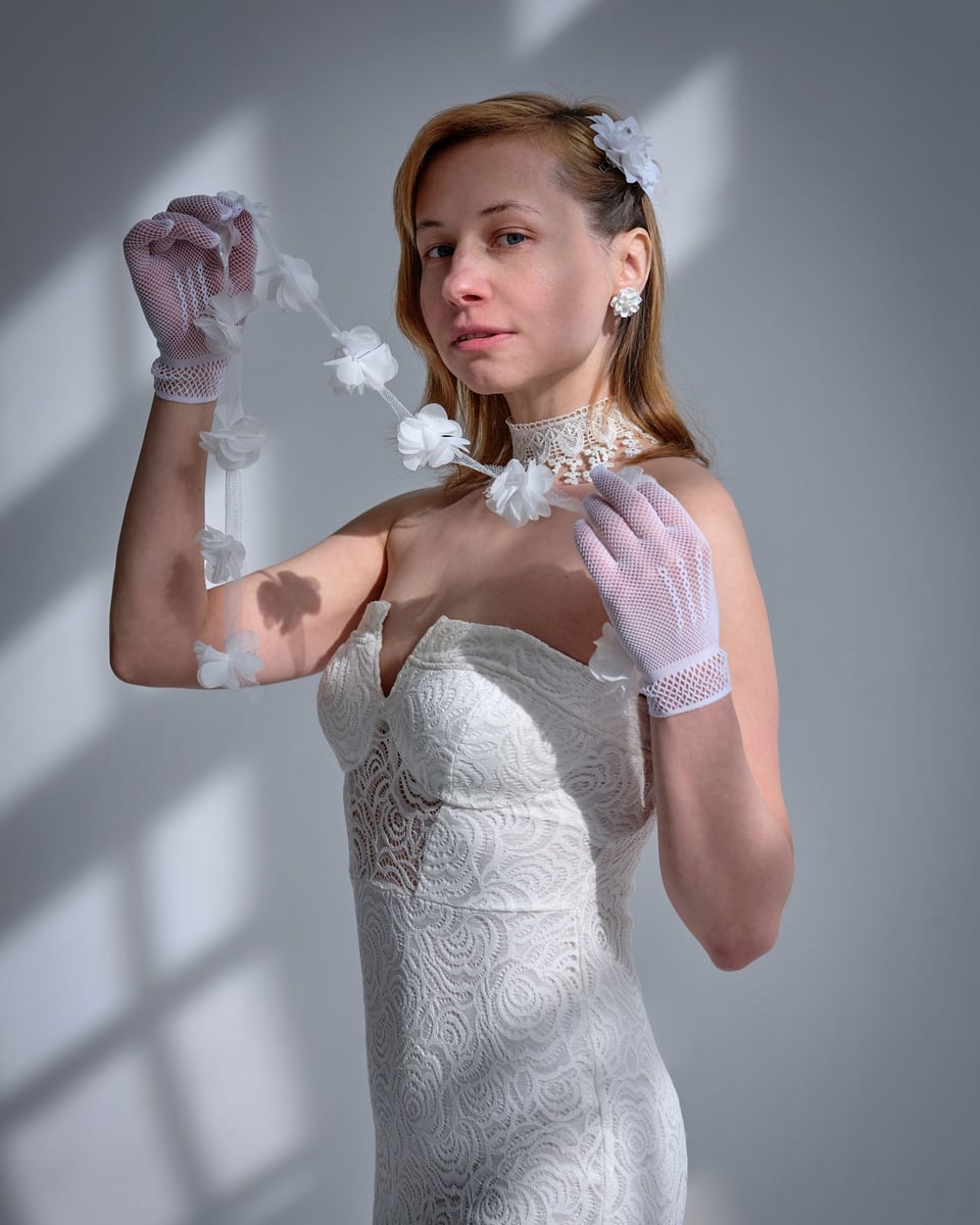 Illustrative photograph of a bride wearing a fitted white dress and gloves in natural studio light.